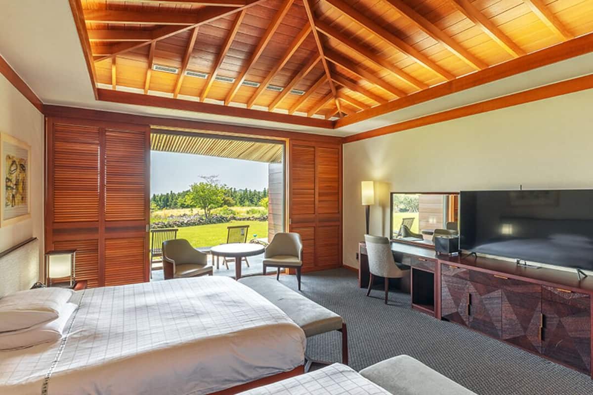 A hotel room with a large bed, a desk with a TV, and a balcony with chairs.