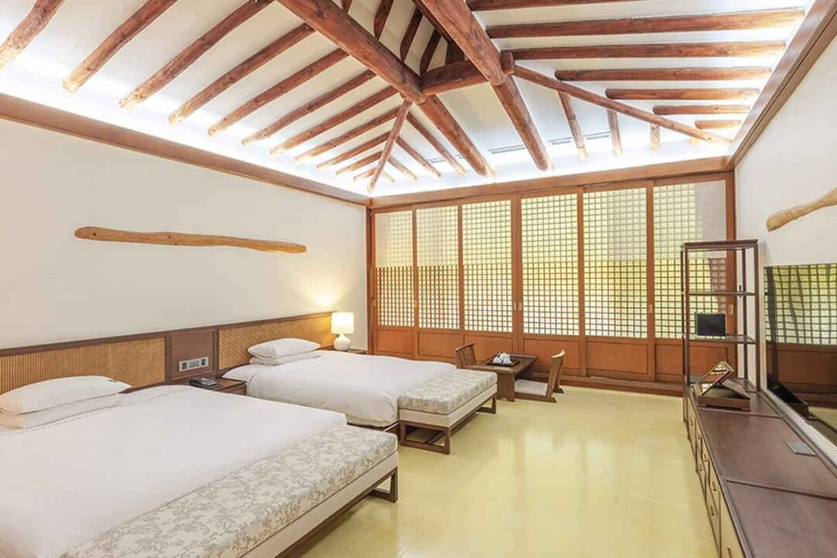 A traditional Japanese-style room with two beds, a wooden ceiling, sliding shoji screens, and a small table with a chair.