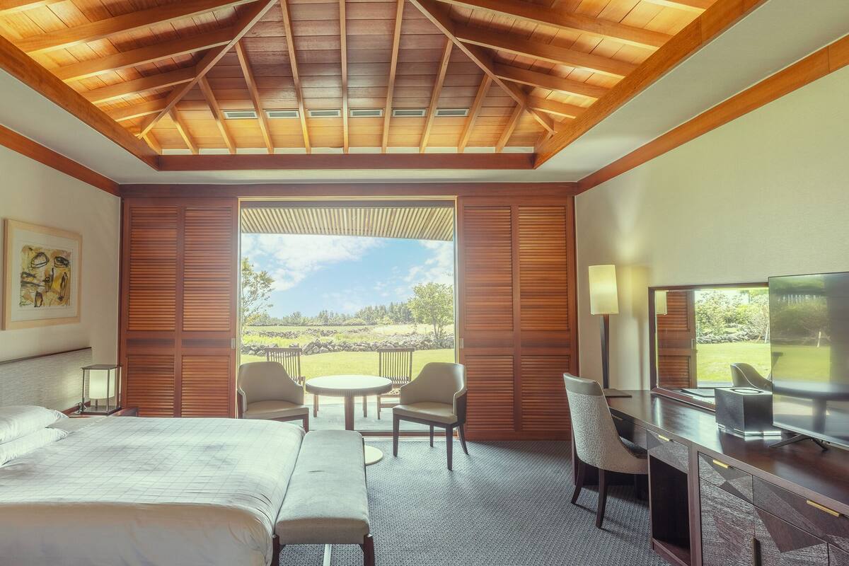 A hotel room with a large bed, a desk with a TV, a chair, and a view of the outdoors.