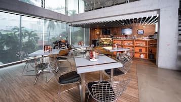 Un restaurante moderno con mesas altas y sillas de malla metálica, amplias ventanas con vista a la ciudad y una motocicleta a la vista.
