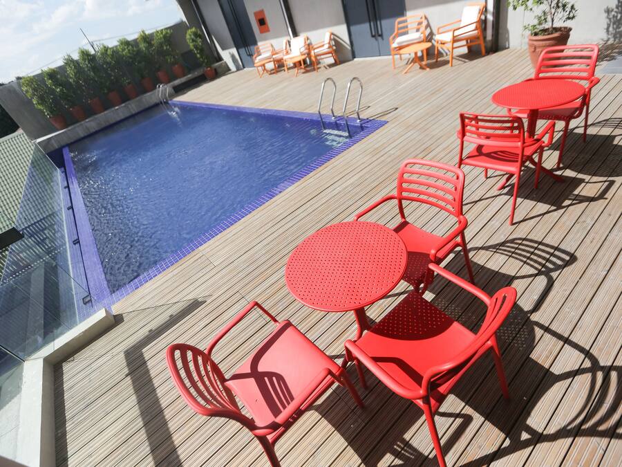 A rooftop pool area with red chairs and tables, a swimming pool, and a view of the city skyline.