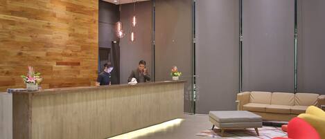Un área de recepción moderna con pared de madera, mostrador de recepción, un sofá y una silla roja.