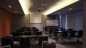 A conference room with a large screen, multiple tables, and chairs arranged for a meeting.