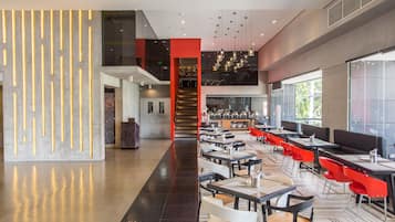 A modern restaurant with a central staircase, multiple dining areas, and a mix of red and black chairs.
