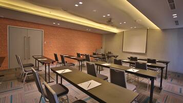 A conference room with tables, chairs, a projector screen, and a brick wall.