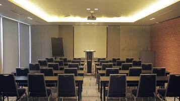 Ein Konferenzraum mit Tischen und Stühlen, einem Projektor und einer Präsentationsleinwand.
