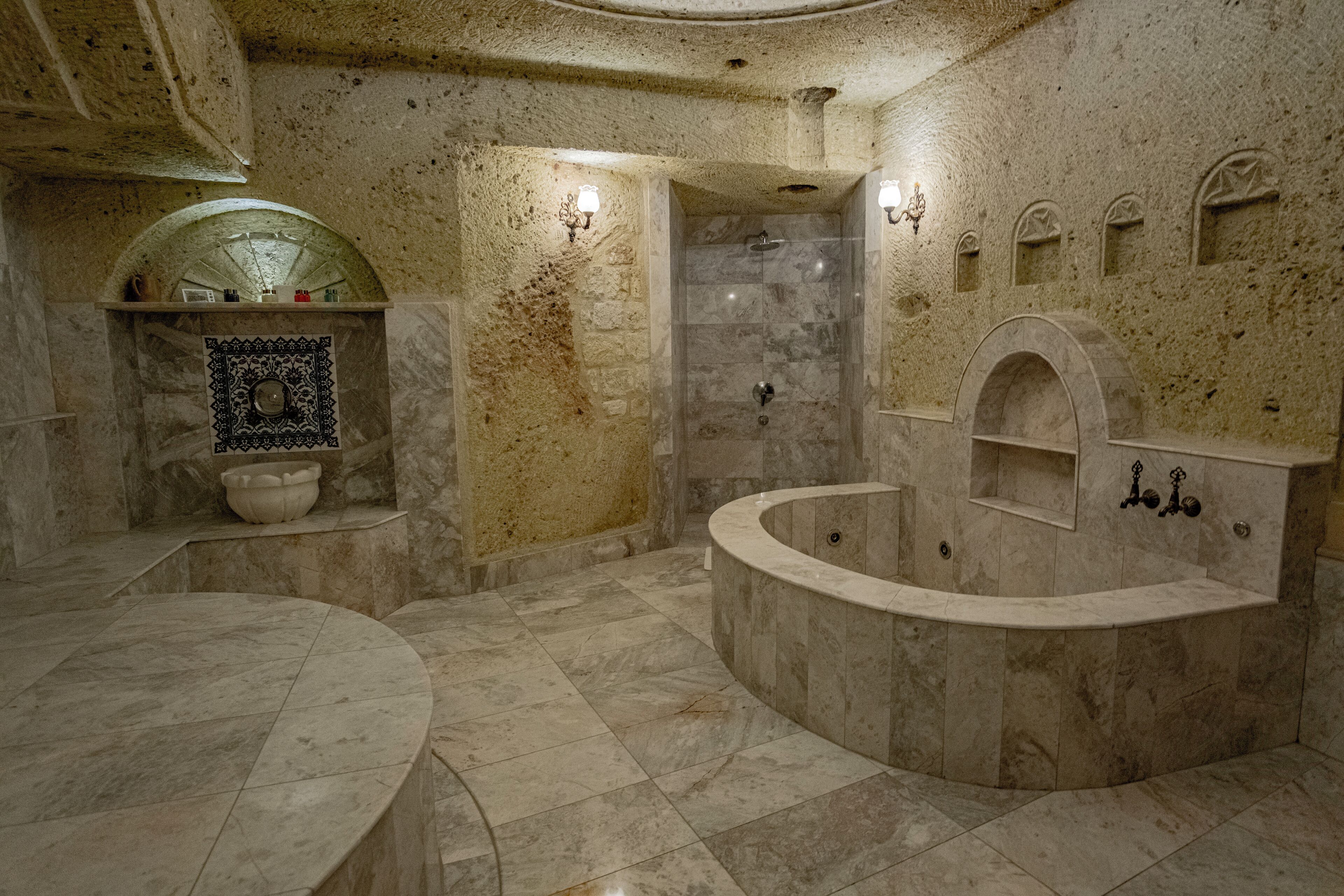 Une salle de bain luxueuse avec un sol en marbre, une baignoire sur pieds, un espace douche et un mur décoratif orné de mosaïques.