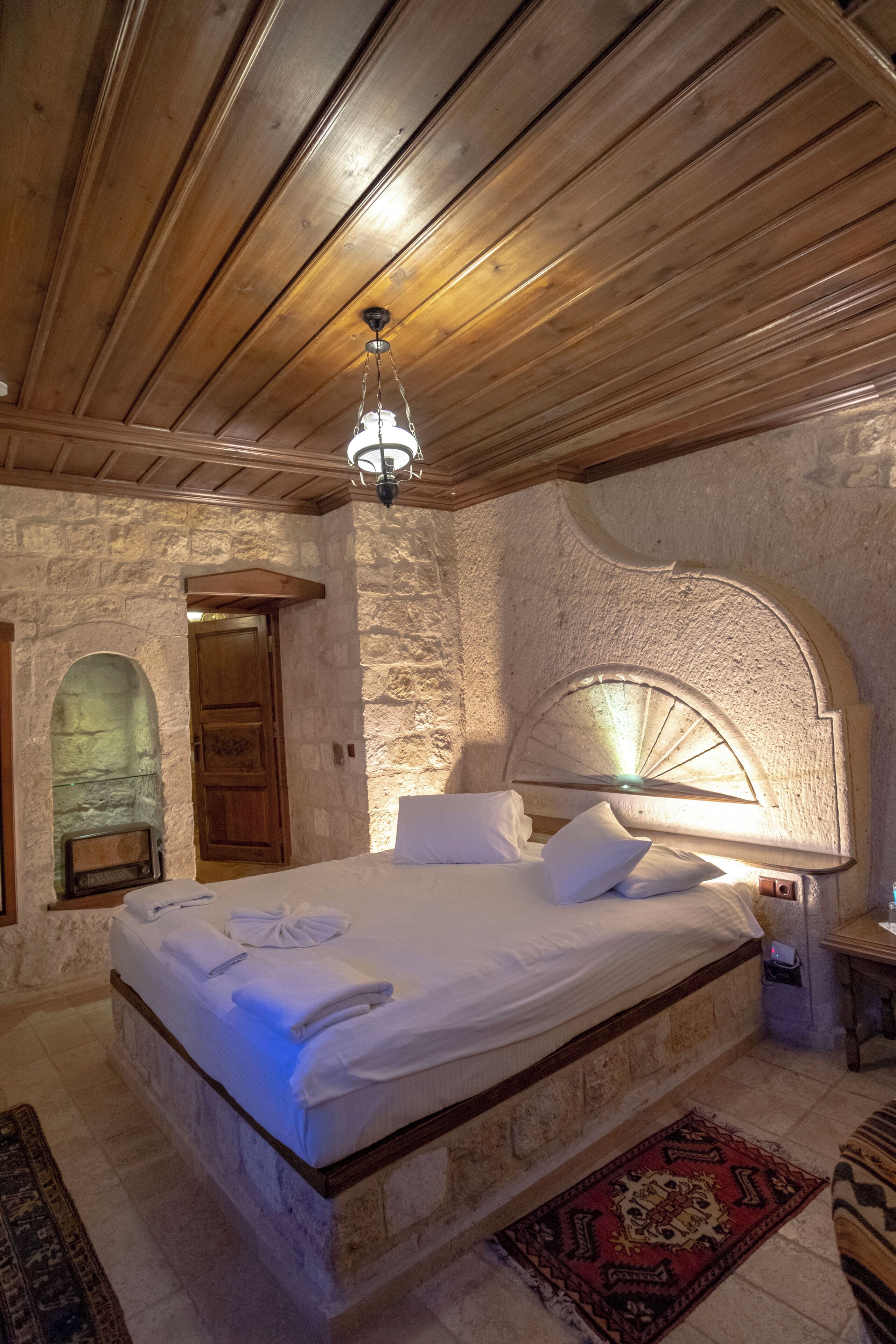 A bedroom with a stone wall, wooden ceiling, and a bed with white linens.