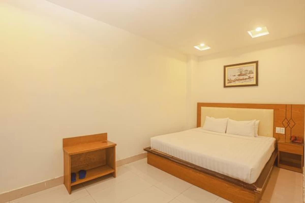 A bedroom with a bed, a nightstand, a wooden shelf, and a framed picture on the wall.