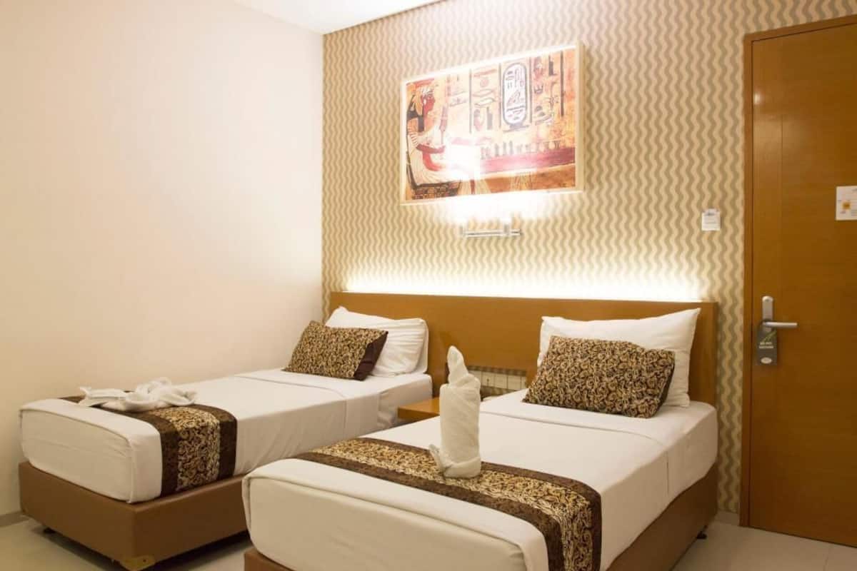 Habitación de hotel con dos camas individuales, cabecera con panel decorativo y puerta de madera.
