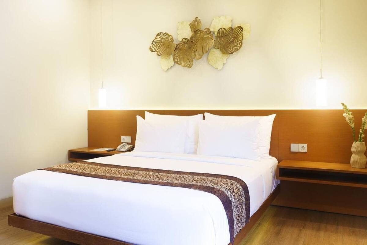 Una habitación de hotel con cama, mesitas de noche, una lámpara de pared y un adorno en la pared.