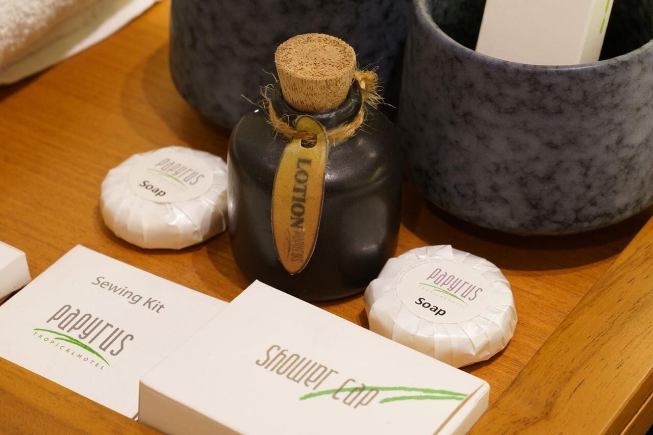A wooden table with a black bottle labeled 'Lotion', two white soap bars, and a 'Sewing Kit' box.