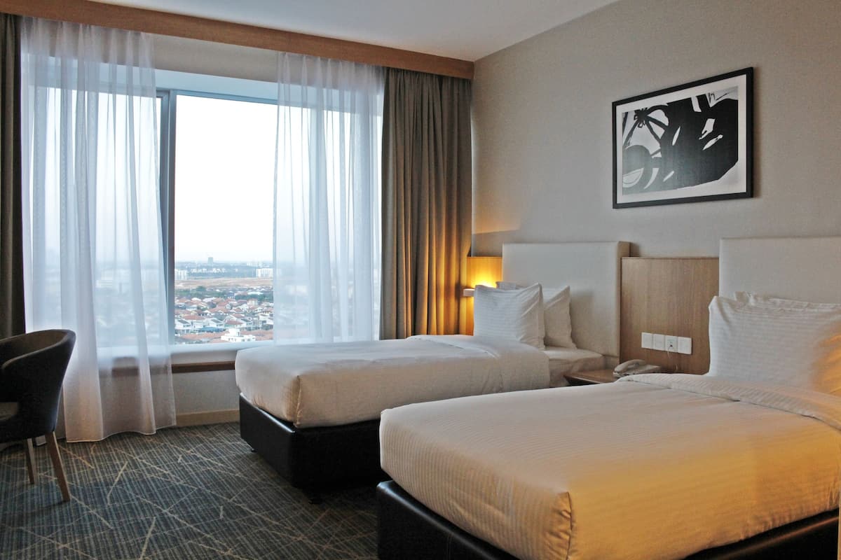 A hotel room with two beds, a chair, a large window with curtains, and a city view.