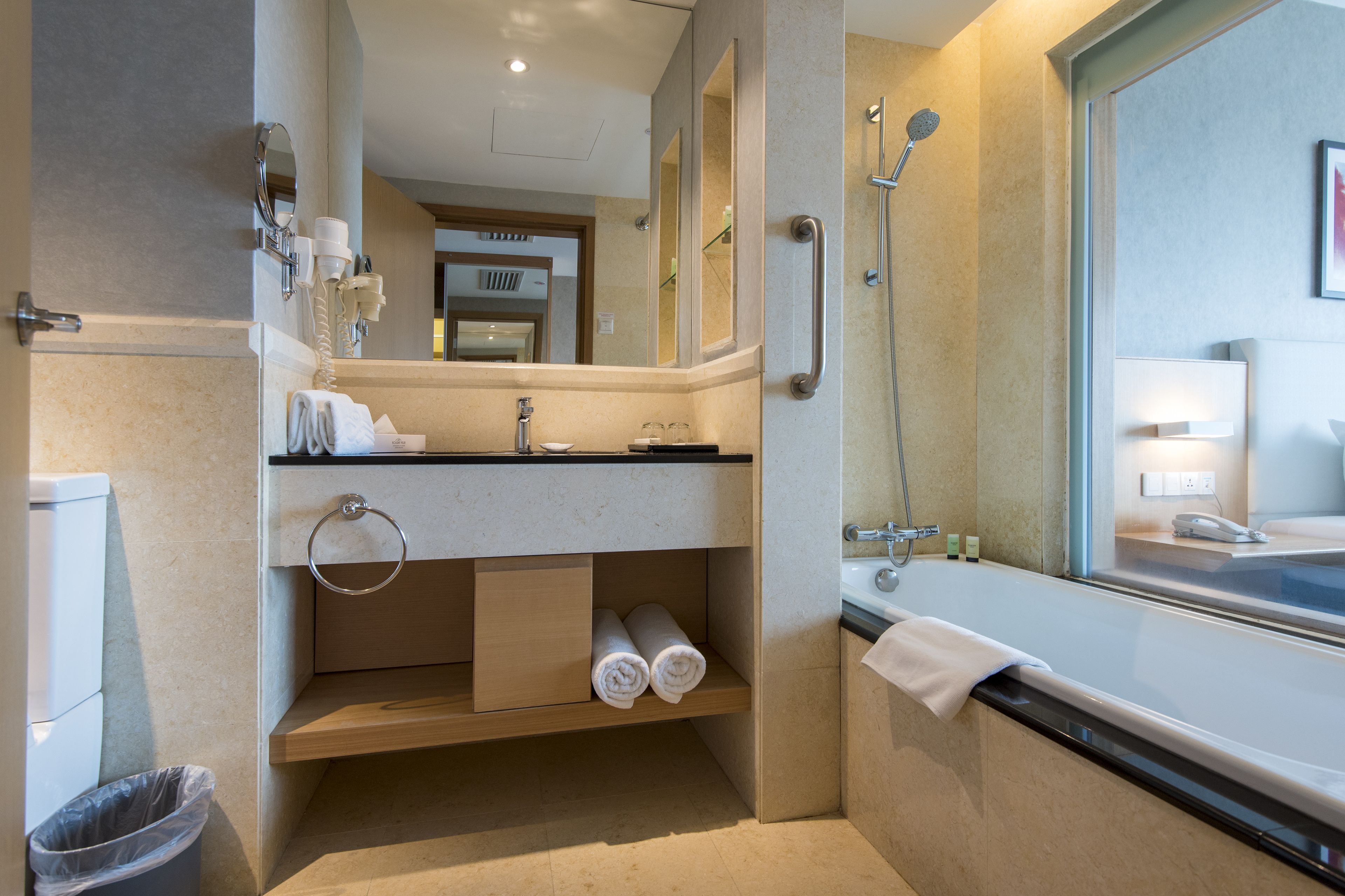 A modern bathroom with a bathtub, a sink with a mirror, a towel rack, and a trash bin.