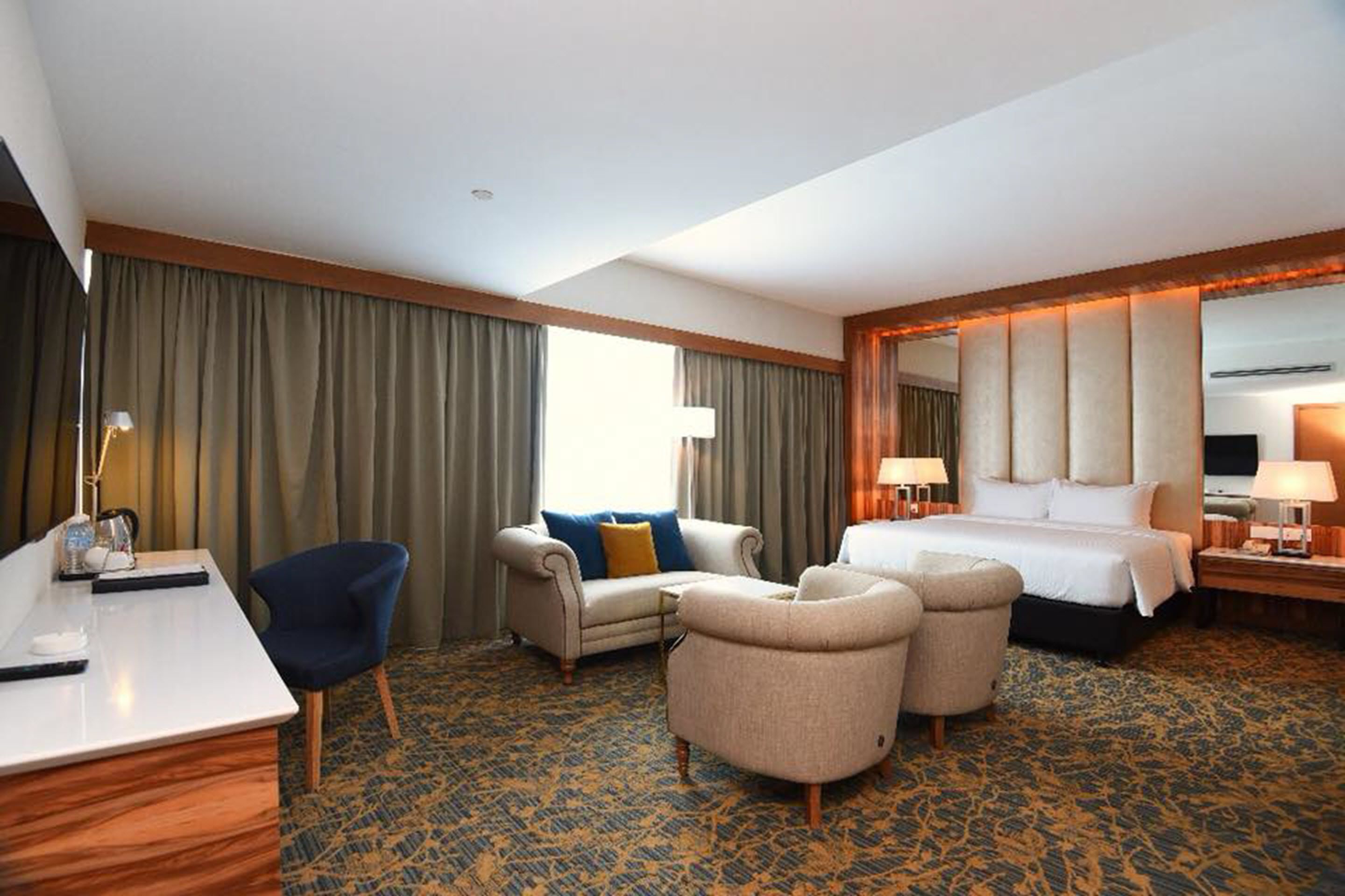 A hotel room with a bed, two armchairs, a sofa, a desk, and a large mirror.