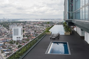 A rooftop pool with a city view, lounge chairs, and a glass railing.