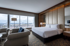 A hotel room with a large bed, a sofa, a desk, and a view of the city.