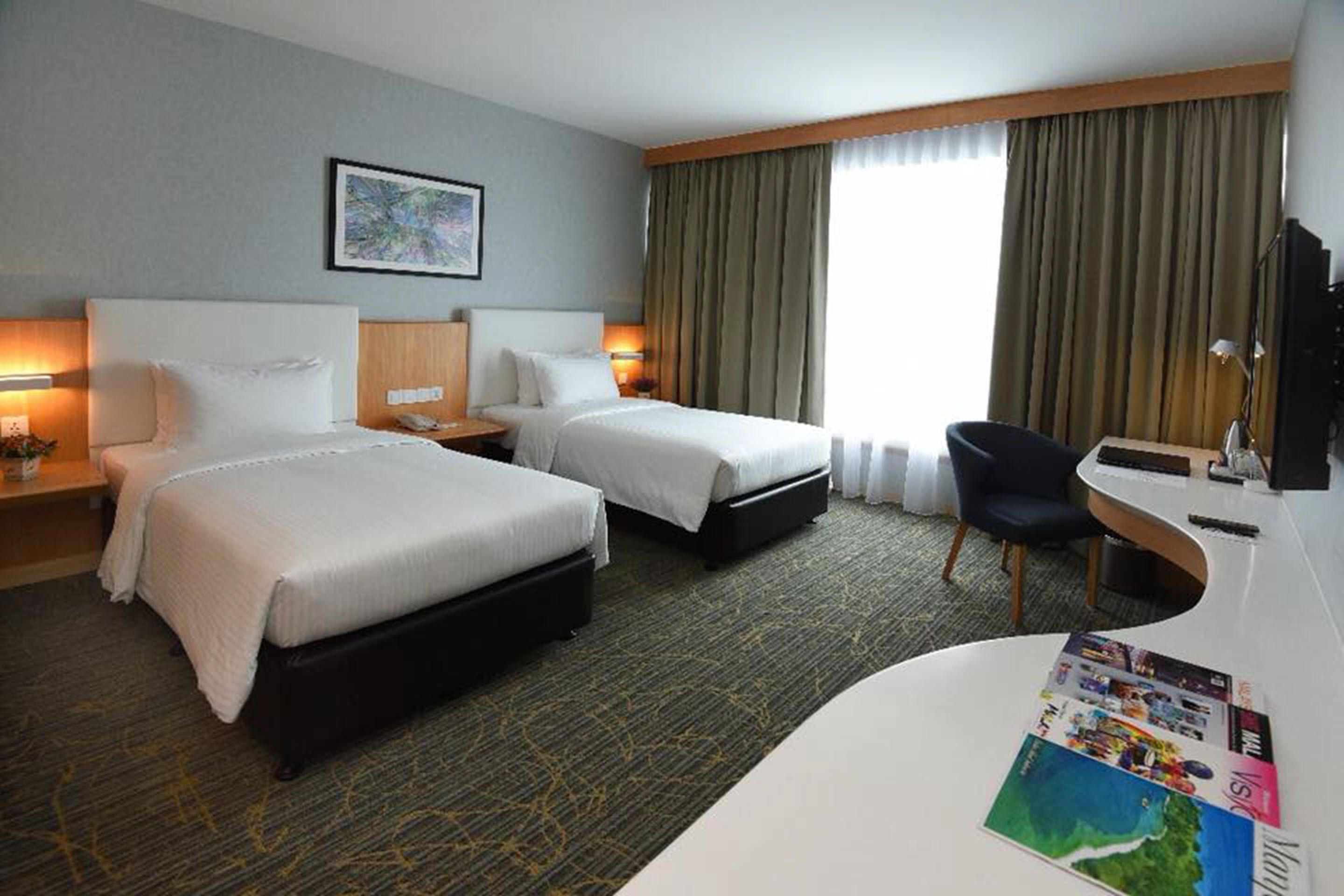 Et hotelværelse med to senge, et skrivebord, en stol og et stort vindue med gardiner.