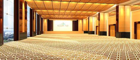 A spacious hotel lobby with a patterned carpet, a high ceiling with a geometric design, and a large window offering a view of the city.