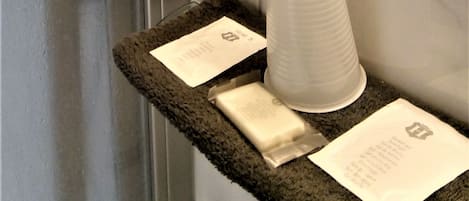 A bathroom with a towel rack, a stack of white paper towels, and a white cup on a textured mat.