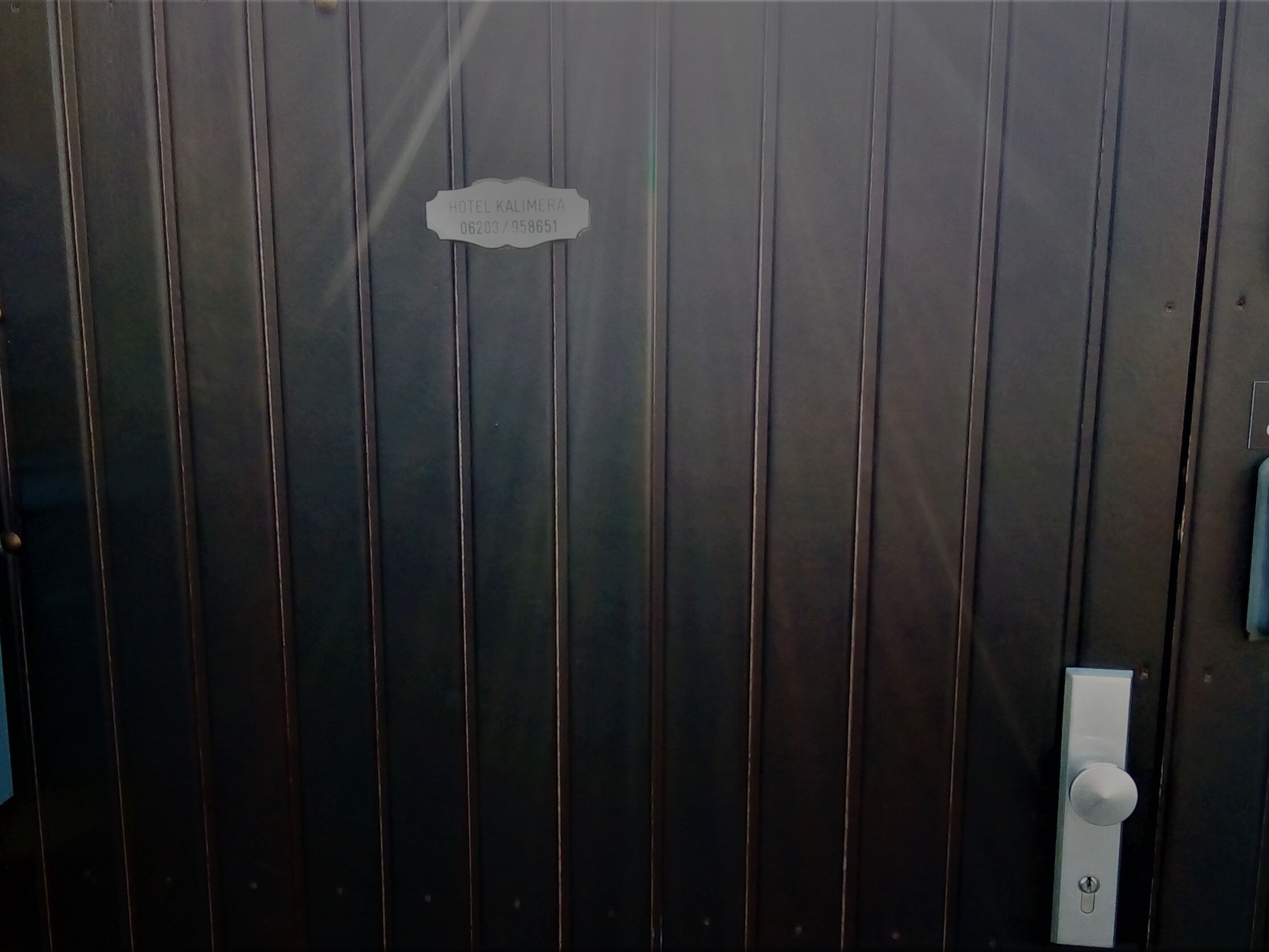 A dark wooden door with a sign that reads "HOTEL KALIMERA 06203 / 958651".