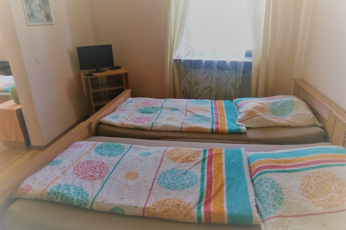 A small room with two beds, a TV on a stand, and a window with curtains.
