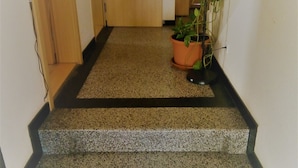 A carpeted hallway with a potted plant and a black-framed staircase. - Hotel Kalimera (Heddesheim)