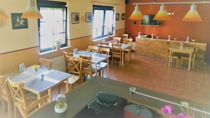 A restaurant interior with multiple tables and chairs, a brick counter, and hanging pendant lights. - Hotel Kalimera (Heddesheim)