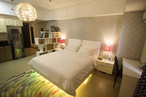 A modern hotel room with a large bed, bedside tables, a red lamp, a white wardrobe, and a kitchenette in the background. - MaxStays Max Style at The Venice Residences (Taguig)