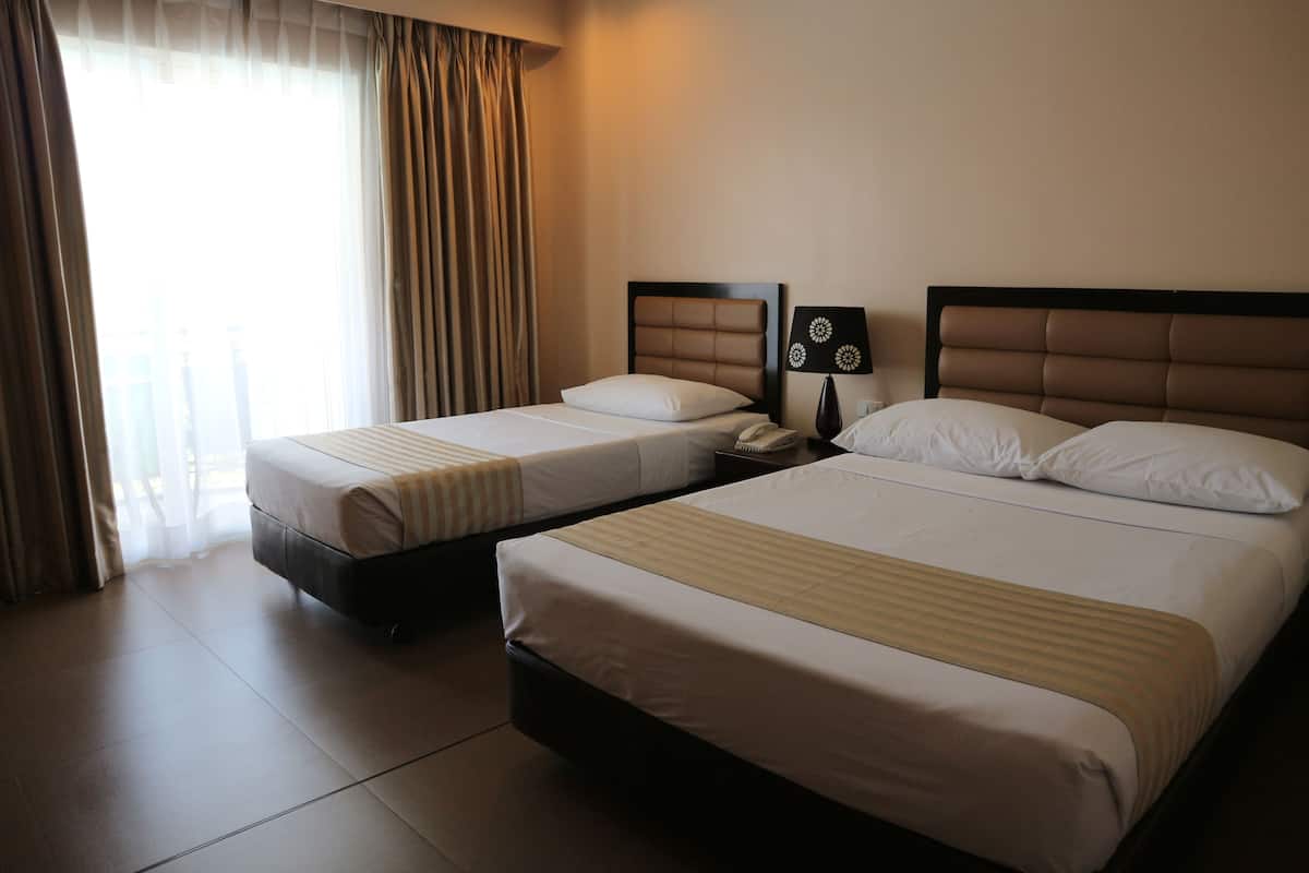 A hotel room with two beds, a nightstand, a lamp, and a window with curtains.