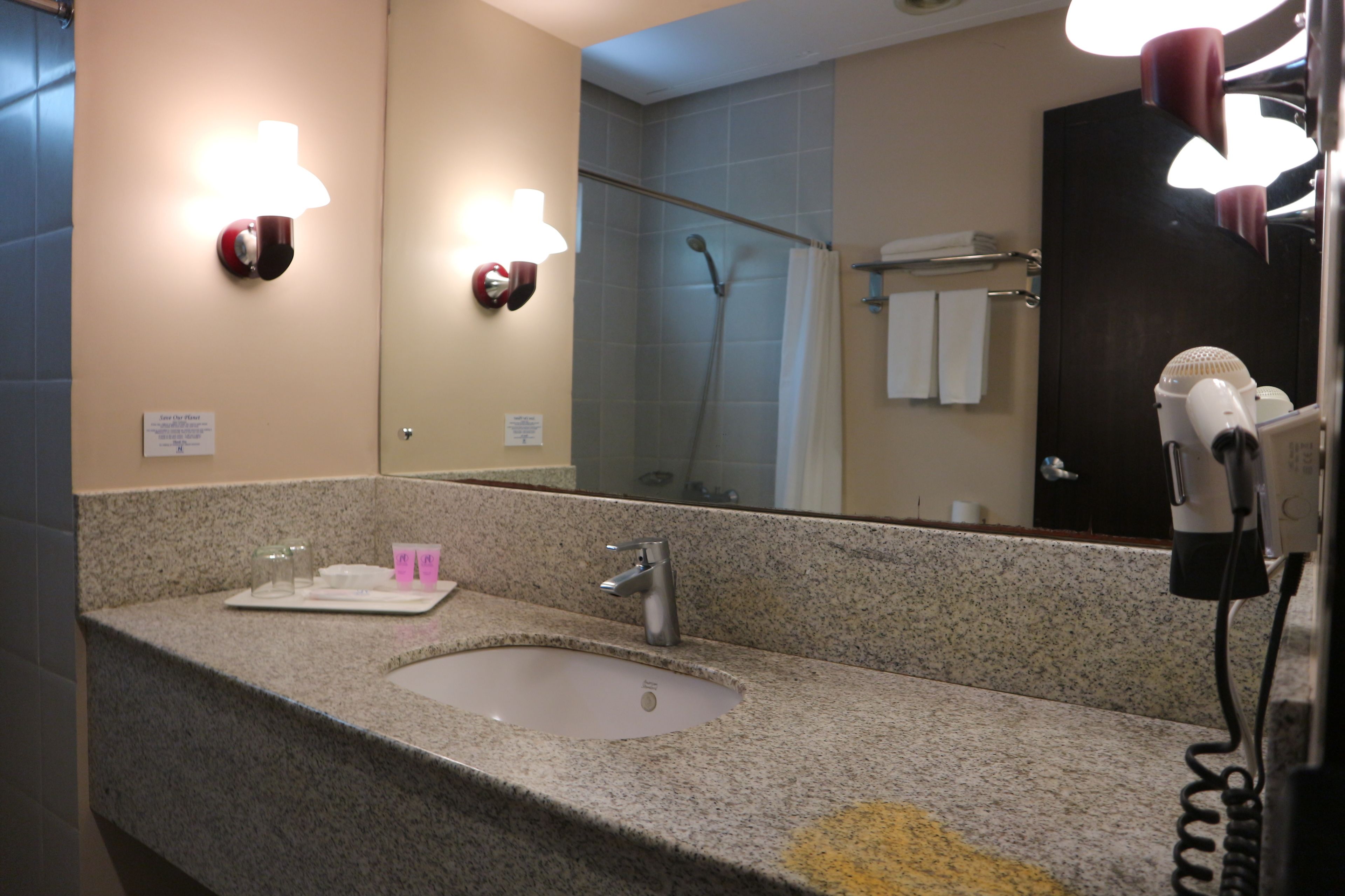 A bathroom with a granite countertop, a sink, a mirror, and a hairdryer.