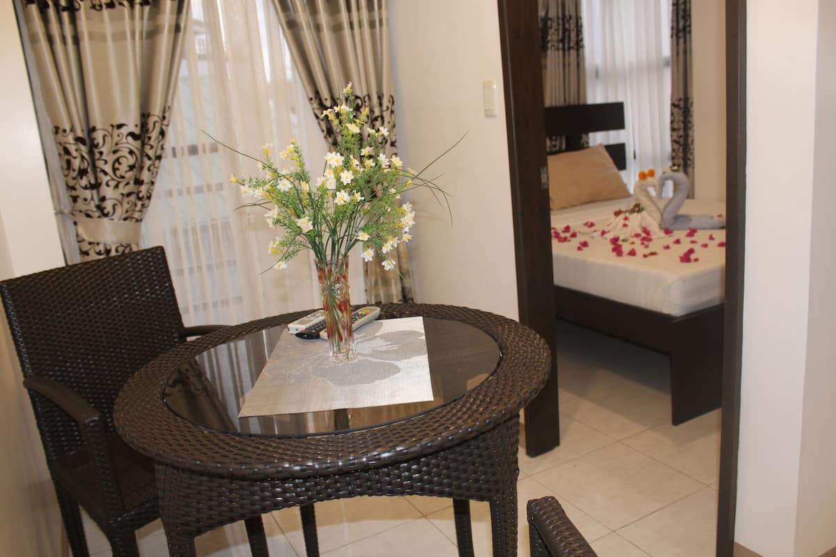 A room with a round dining table, two chairs, a vase with flowers, a bed with rose petals, and a swan decoration.