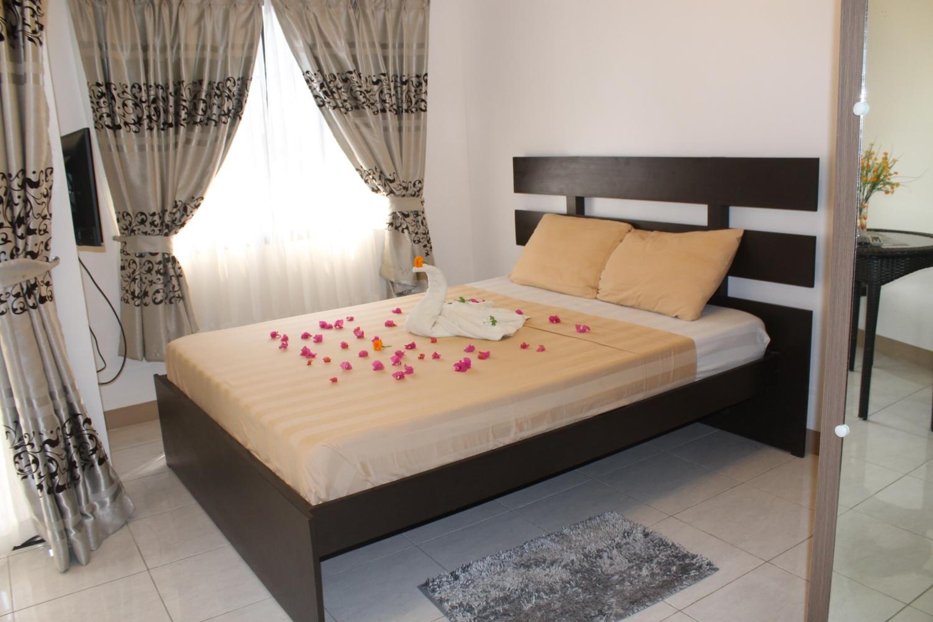 A neatly made bed with a beige and white bedspread, a brown headboard, and a small rug on the floor.