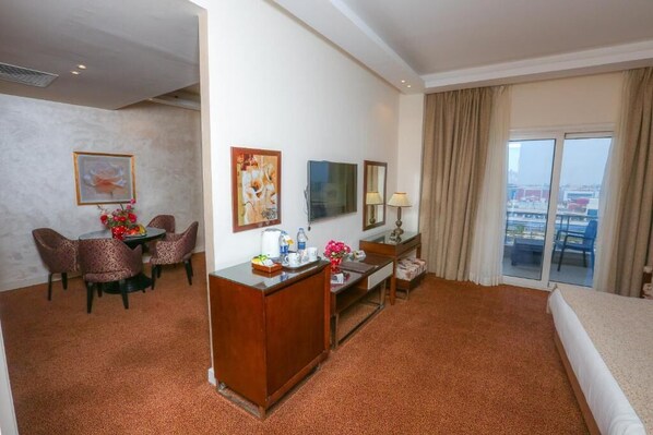Habitación de hotel con cama, escritorio con silla, mesa de comedor con sillas, televisor y vistas a la ciudad a través del ventanal.