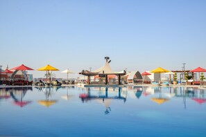 Una piscina con sombrillas y sillas de descanso, reflejando el cielo despejado.