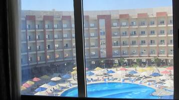 A hotel with a pool area, multiple floors, and a large building in the background.