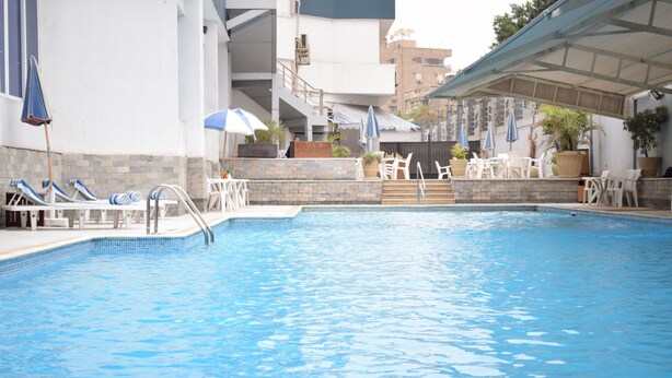 A swimming pool with lounge chairs and umbrellas, surrounded by a stone wall and potted plants.