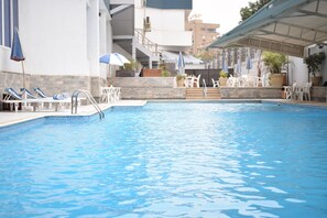 A swimming pool with lounge chairs and umbrellas, surrounded by a stone wall and potted plants. - Tolip Inn Maadi (Cairo)