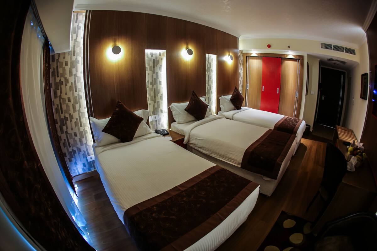 A hotel room with two beds, a wooden floor, a red door, and a small table with fruits.