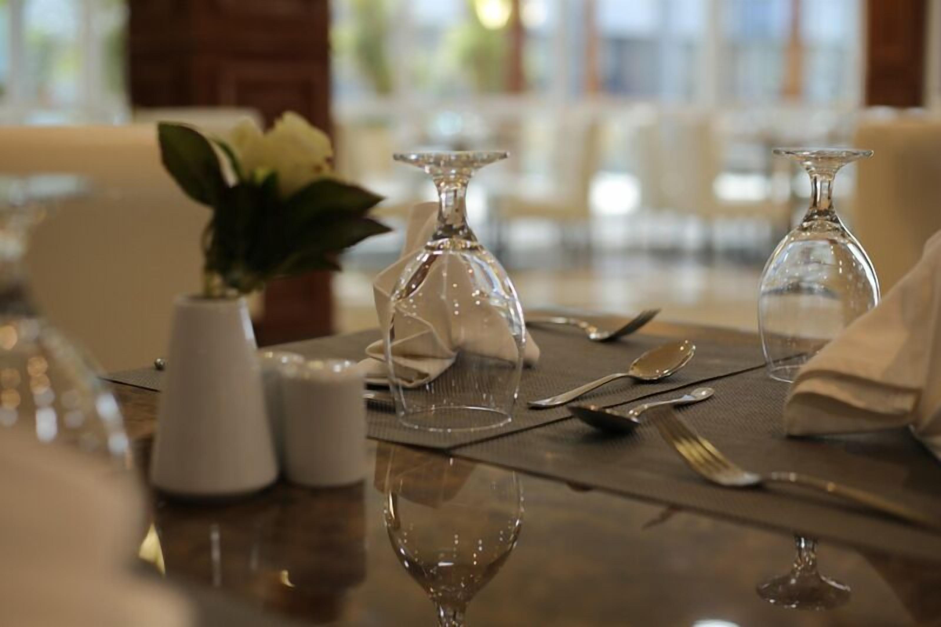 Una mesa de comedor con cristalería transparente, un florero con flores blancas y saleros y pimenteros.