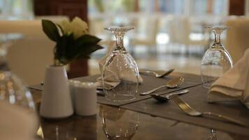 Una mesa de comedor con cristalería transparente, un florero con flores blancas y saleros y pimenteros.