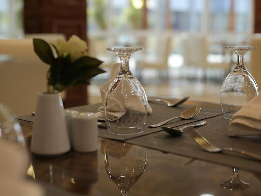 Una mesa de comedor con cristalería transparente, un florero con flores blancas y saleros y pimenteros.