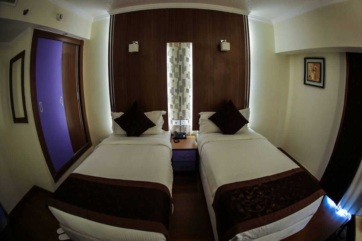 A hotel room with two beds, a nightstand with a telephone, and a mirror on the left wall.