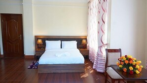 A hotel room with a large bed, two bedside tables with lamps, a wooden door, a chair with a vase of flowers, and a patterned curtain. - Gentle Hotel (Addis Ababa)