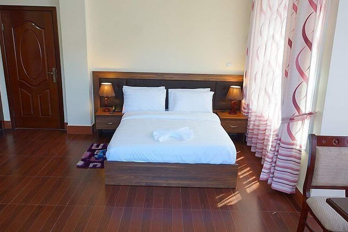 A neatly made bed with white linens, two bedside tables with lamps, a wooden headboard, and a patterned curtain.