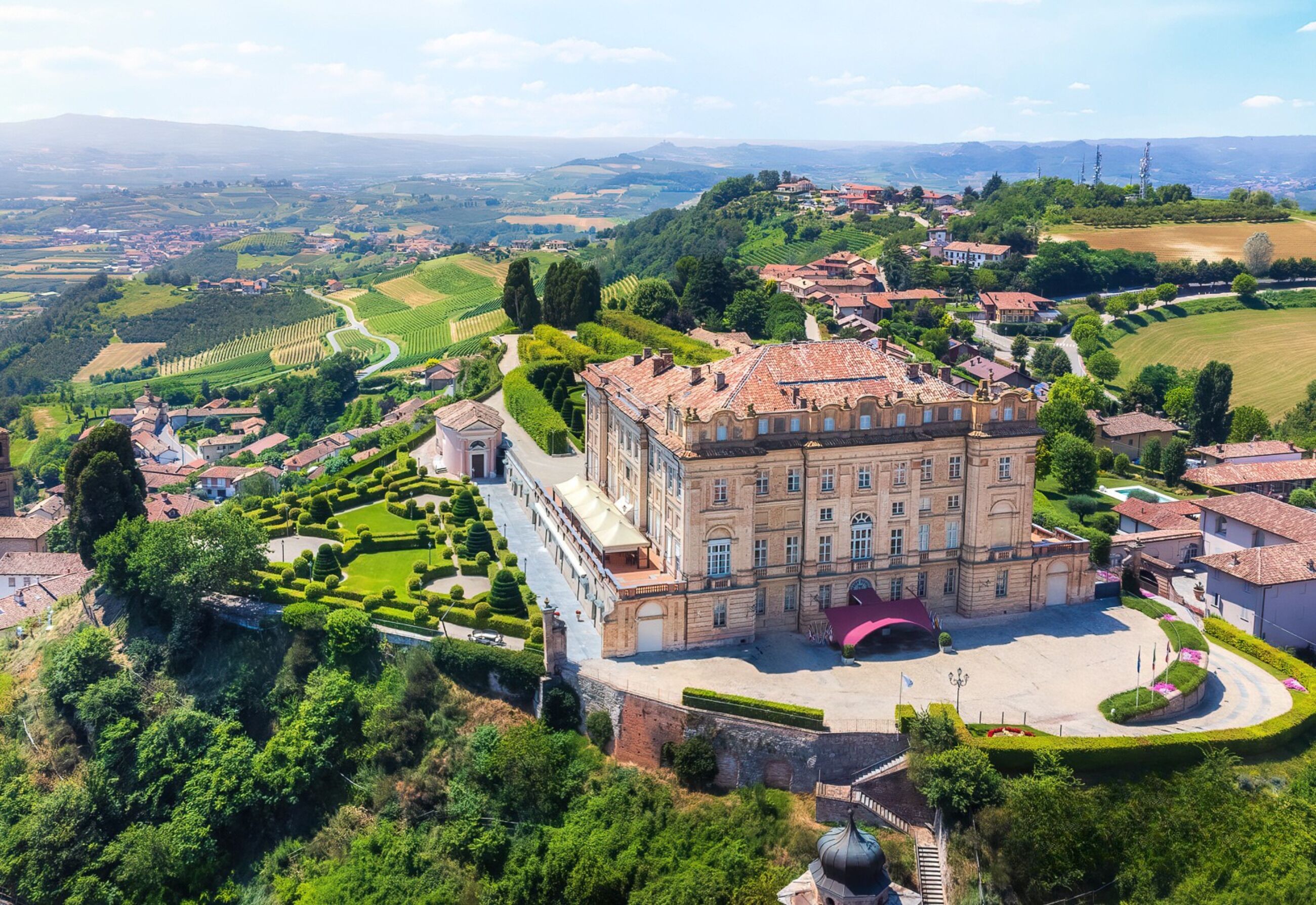 A historic building with a central courtyard, surrounded by well-maintained gardens and a hilly landscape.