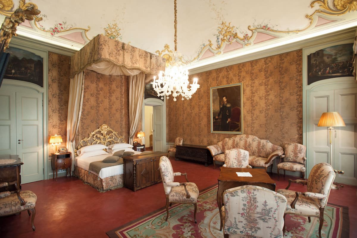 Ein Zimmer mit einem großen Bett, einer Kandelaber, einer Sofagarnitur und einem Gemälde an der Wand.
