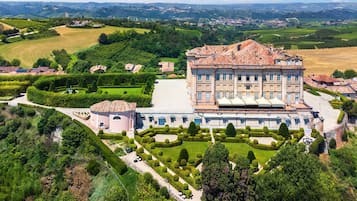 A large, historic building with a symmetrical facade, surrounded by well-manicured gardens and a hilly landscape.