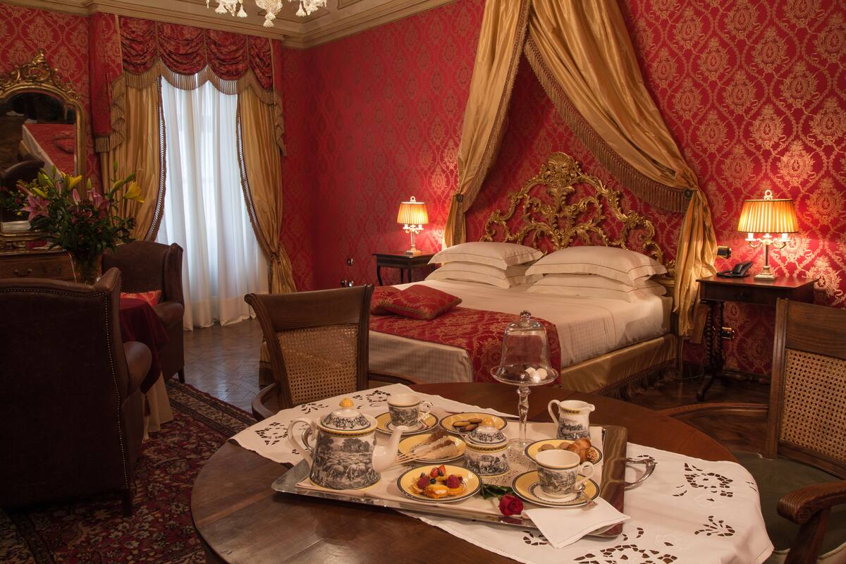 Ein luxuriöses Schlafzimmer mit einem großen Bett, aufwendigen Vorhängen und einem Esstisch, gedeckt mit Teegebäck.
