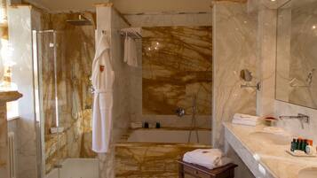 Un bagno moderno con doccia vetrata, parete rivestita in marmo, vasca da bagno e mobile lavabo con articoli da toilette.